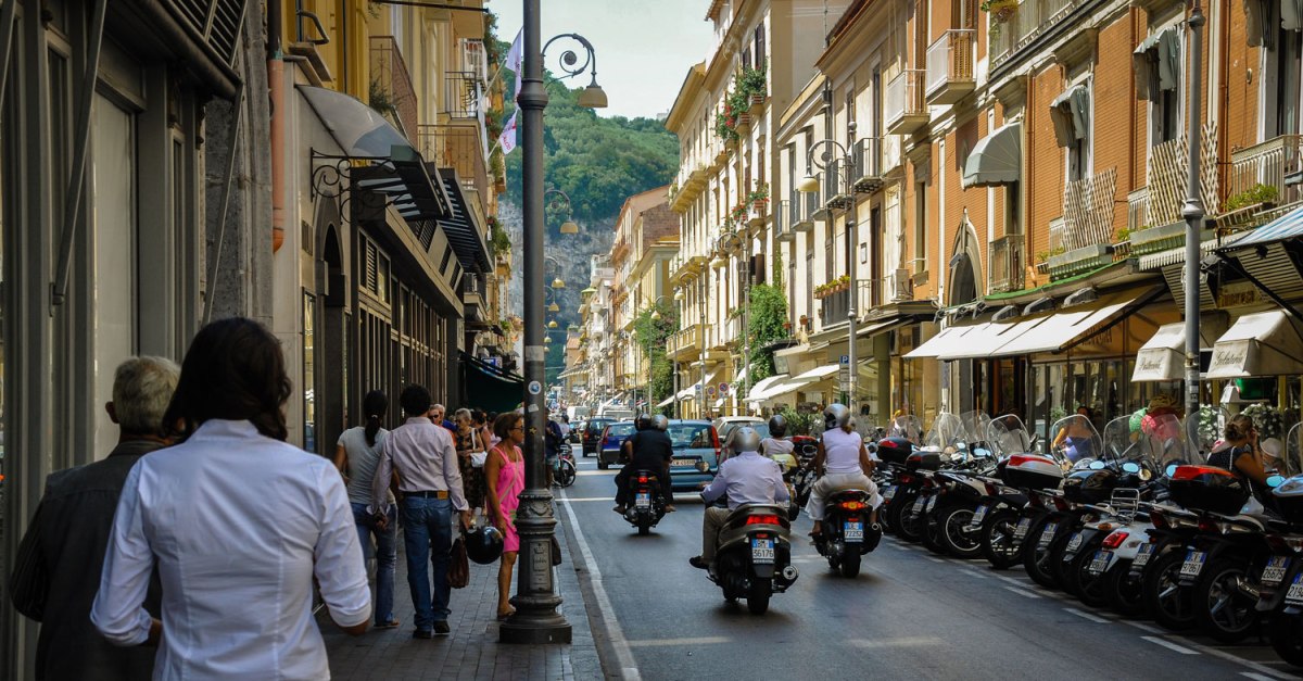 A busy street in Sorrento, filled with pedestrians and parked motorcycles and people riding motorcycles.