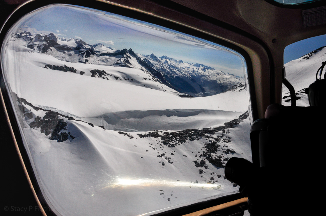 From inside the cockpit of a helicopter, stunnings views of snow-capped mountains, near and far.