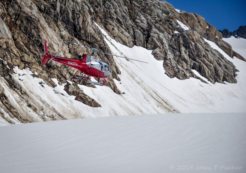 Helicopter Takeoff; Photo: SPFischer Red helicopter against a backdrop of snow, sheer rock, and blue skies.