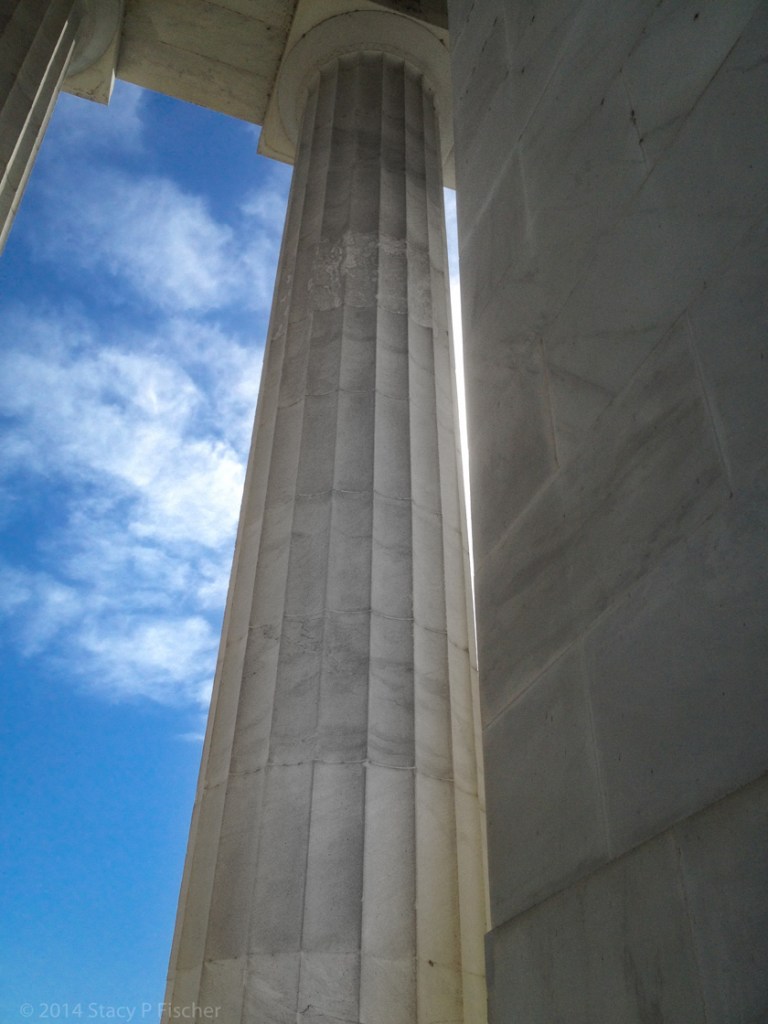 Looking up the height of the column to the top, framed on the left against a deep blue sky and white clouds.