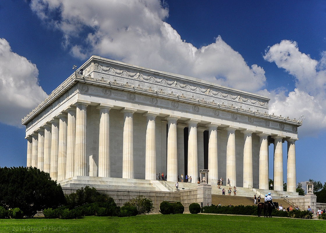 The east and south facades of the Lincoln Memorial, framed against a deep-blue sky dotted with white clouds.