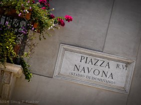 Piazza Novona Street sign in carved stone on the corner of a building, with a flowered balcony to the left.