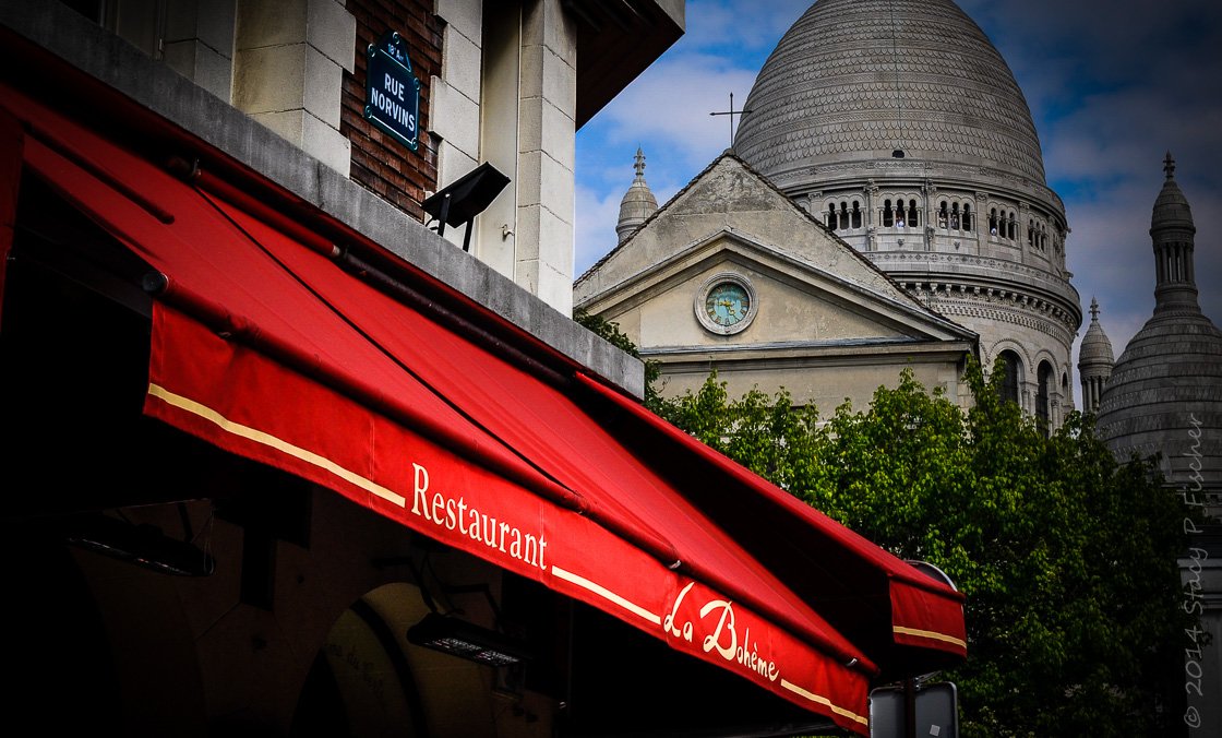 Red canopy of La Bohème Restaurant with a view of Sacré Cœur in the background.