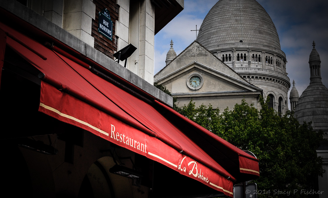 Red canopy of La Bohème Restaurant with a view of Sacré Cœur in the background.