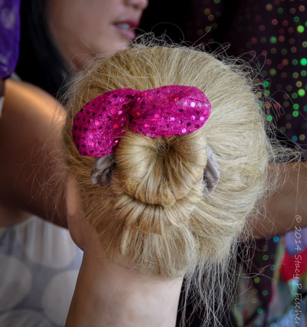 Back of blonde wig on a form fashioned into a ballerina bun with a pink sequined bow.