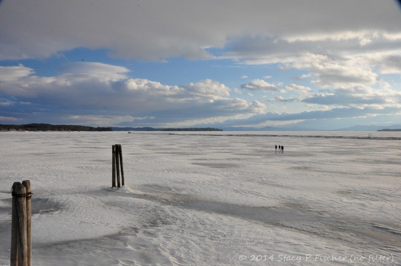 People walking on the frozen surface of Lake Champlain all the way out to the jetty and the lighthouse.