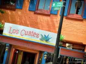 Orange brick, bright blue shutters, red and orange woodworking of Los Cuates Mexican Restaurant.