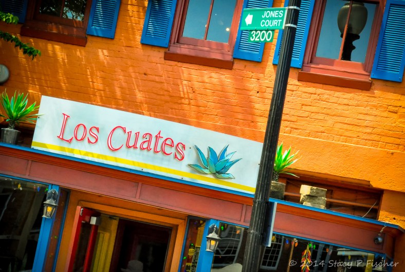Orange brick, bright blue shutters, red and orange woodworking of Los Cuates Mexican Restaurant.