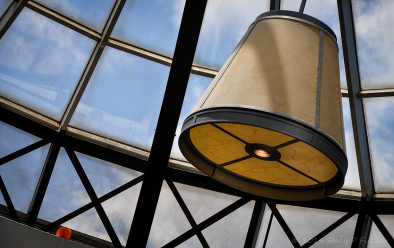 Orange balloon laying on a ledge in a skylight nexxt to a large lighting fixture.
