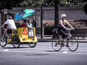 Two passengers in a pedicab heading one direction; another lone cyclicst heading past in the opposite direction.