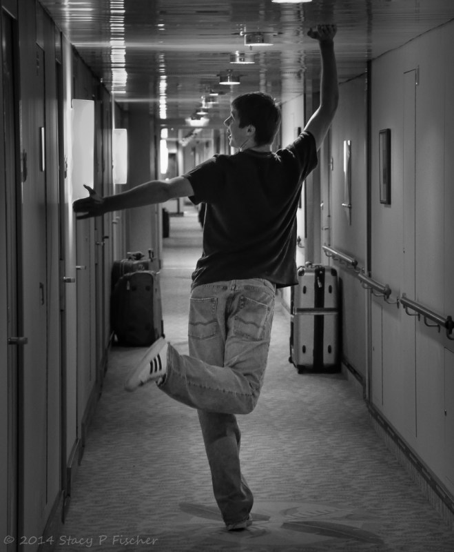 Demonstrating the narrowness of a cruise ship hallway, young man strikes funny pose, touching the ceiling with one hand and the left wall with another.