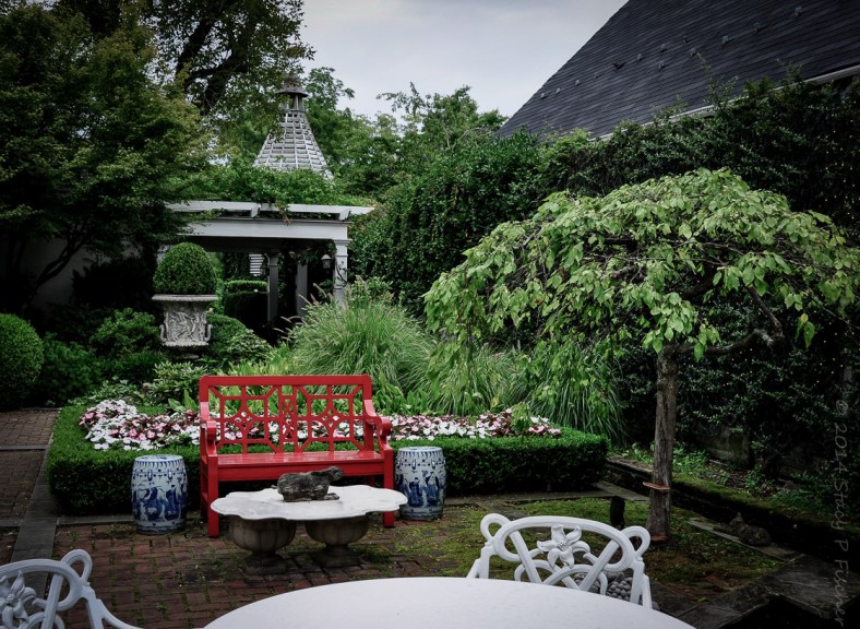 Garden; Photo: SPFischer The garden terrace, with red bench, white tables, lush greenery, and goldfish pond