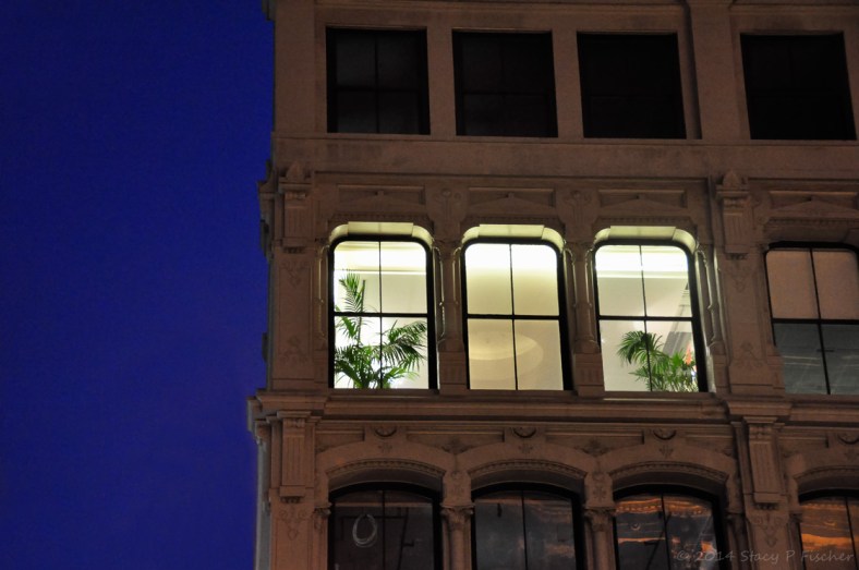 A nighttime view from the street of a brightly lit second story living room.