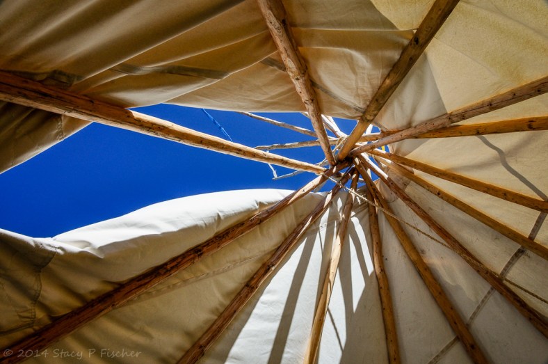 A view inside a teepee looking up to the bright blue sky through the wooden supports. 
