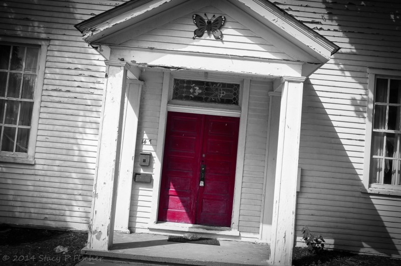 Empty and neglected white wooden building with peeling paint and red double door.