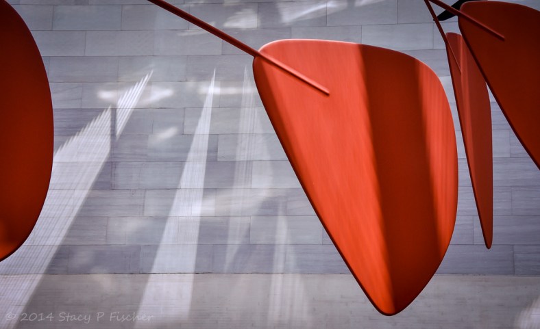 4 orange segments of the mobile framed against the shadowed white brick wall of the atrium.