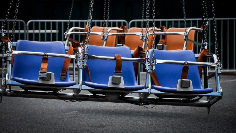One row of 3 empty blue seats in front of one row of 3 empty orange seats on a carnival ride.
