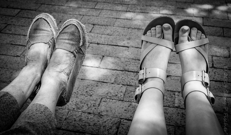 Contrast between two pairs of shoed feet, one elderly and one young teen.