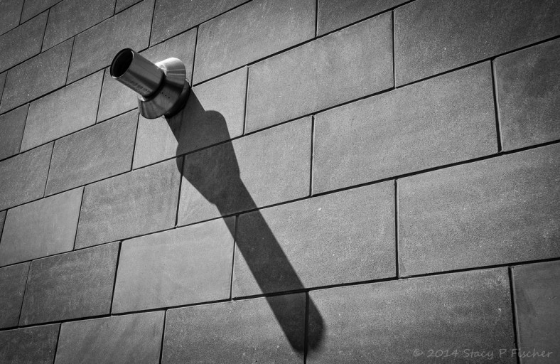 Metal pipe protruding from a brick wall casts a long shadow.