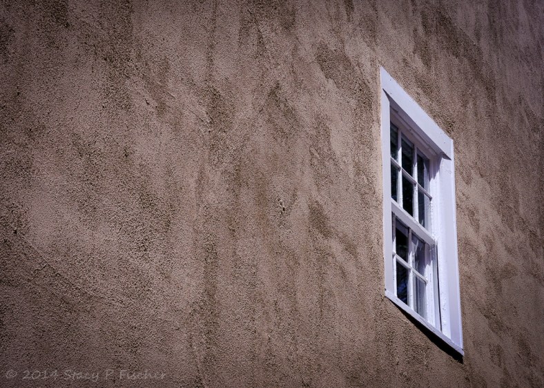 Second-story white window contrasted against a textured brown exterior wall of a house.
