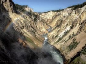 Yellowstone River sporting a rainbow in the foreground winds through canyon after tumbling over Lower Falls.