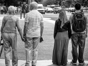 Two couples, one elderly and one young adults, holding hands as they wait to cross the street.