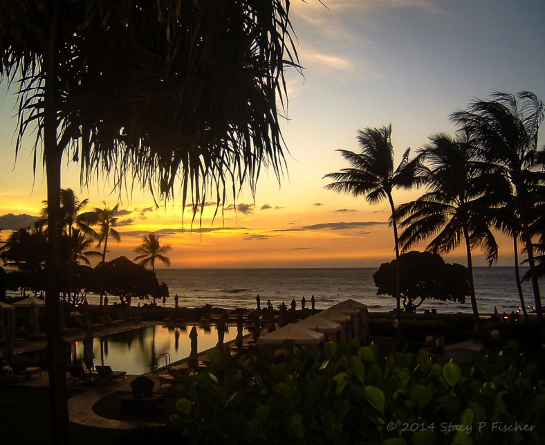 Sunset over beach at Hualalai, Hawaii creates silhouetttes of palm trees, sightseers, swimming pool and cabanas.