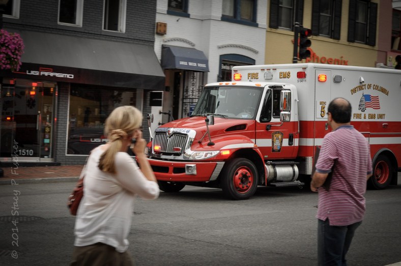 Two onlookers stop on a street corner to watch approaching ambulance