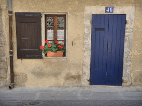 Blue door and red geraniums in window of home in Bonnieux, France