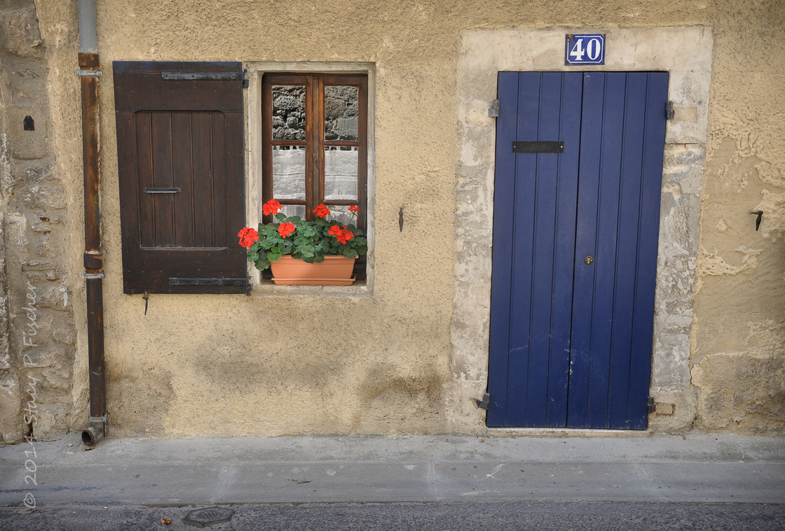 Blue door and red geraniums in window of home in Bonnieux, France