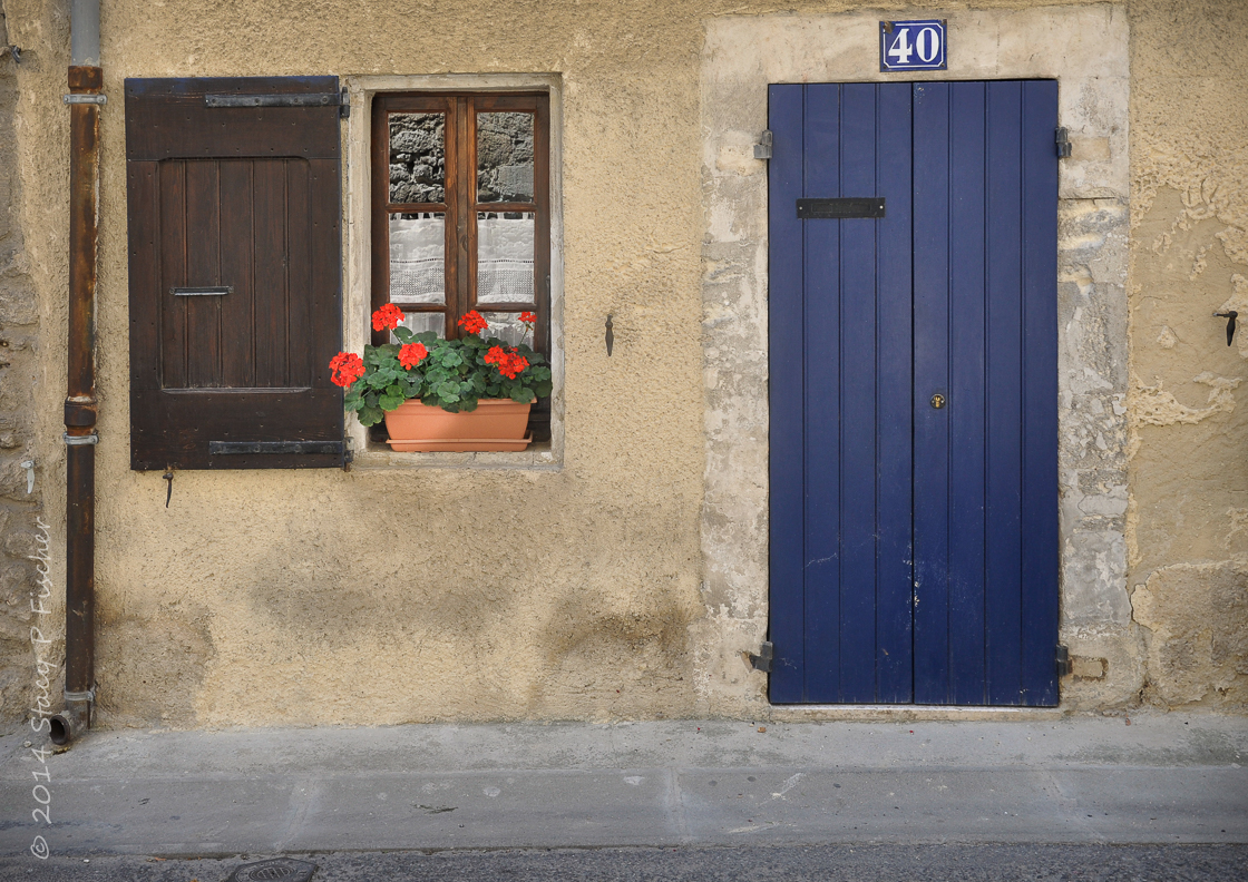 Blue door and red geraniums in window of home in Bonnieux, France