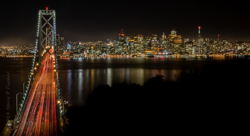 Oakland Bay Bridge at night, against the backdrop of San Francisco ablaze with twinkling lights.