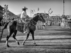 Rodeo cowgirl on horse heading to the arena, against the backdrop of the county fair rides.