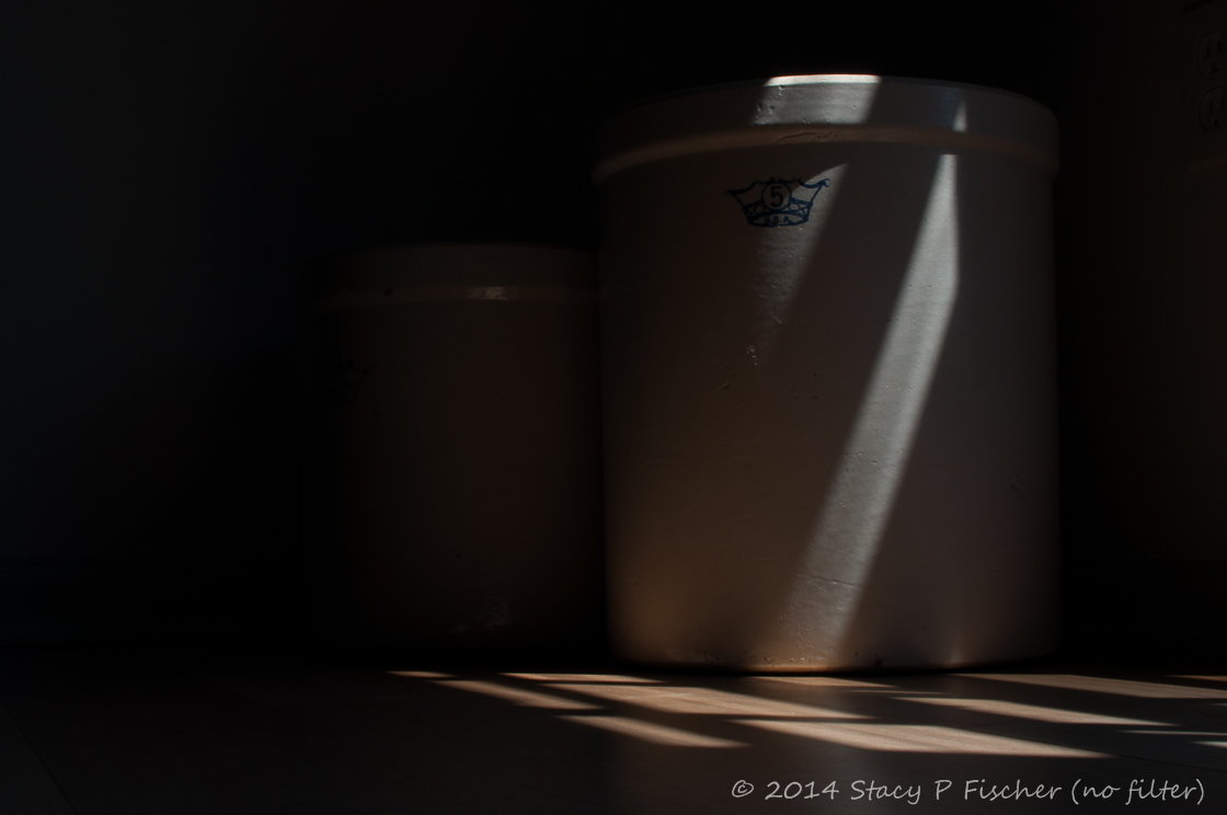 Unedited photo of two stoneware crocks sit in light and shadows from nearby window.