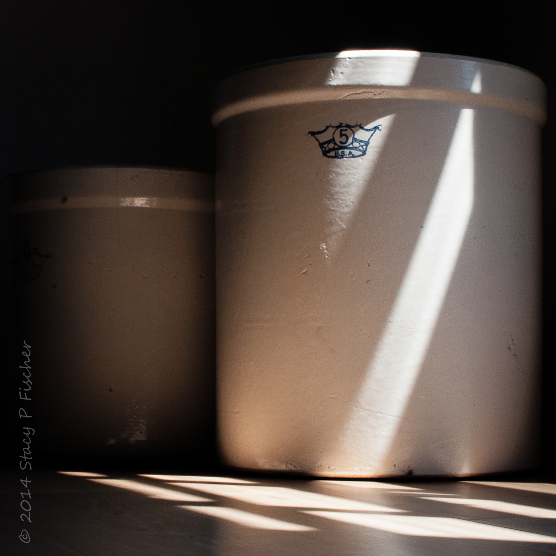 Two stoneware crocks sit in light and shadows from nearby window.