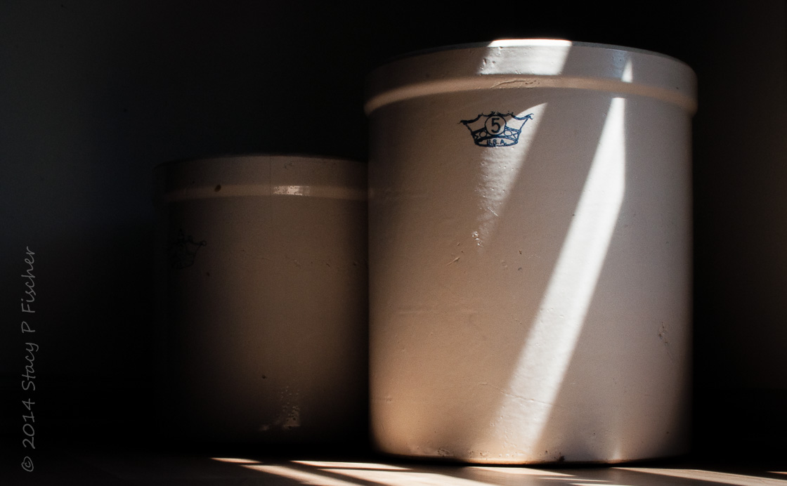 Two stoneware crocks sit in light and shadows from nearby window.