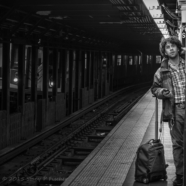Man peering down New York City subway tracks, waiting for next train.
