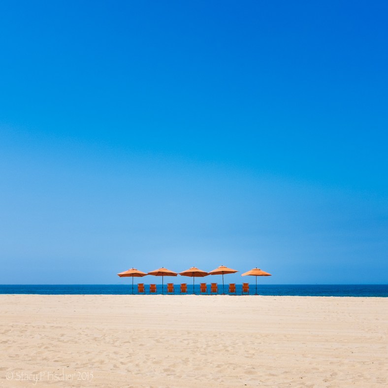 Orange umbrellas and chairs on a beach silhouetted against the bright blue of the sky and water.