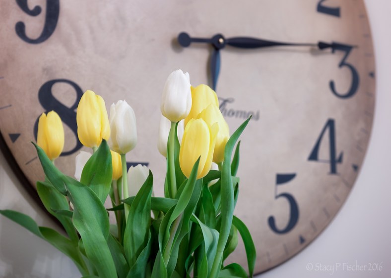 yellow and white tulips against background of clock